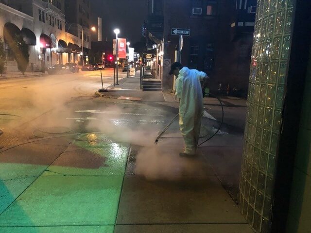 A CKC technician uses a pressure washer to remove gum and dirt from a sidewalk