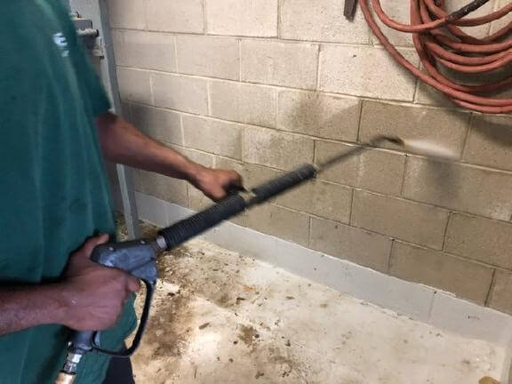 CKC Technician pressure washing wall in a trash room